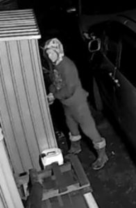 Hooded intruder beside stacked materials on night security camera