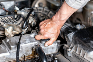 Mechanic's hand topping up engine oil under a car bonnet