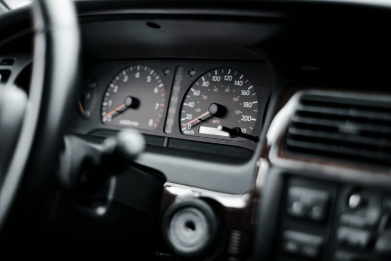 Car dashboard speedometer blurred through steering wheel.