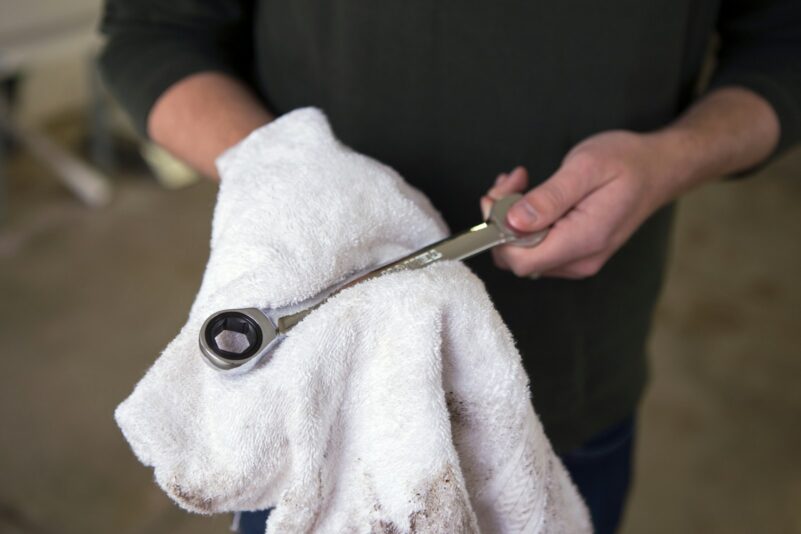 Mechanic holding a ratchet, wiping it clean with a white towel.
