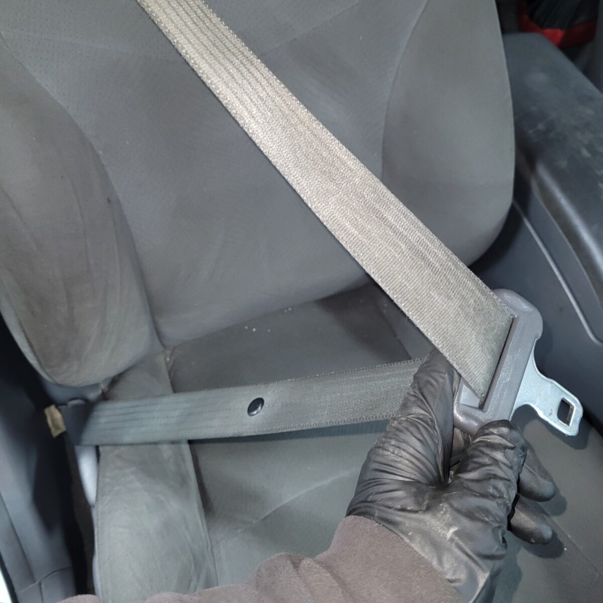 Gloved hand pulling a seatbelt out from a car seat