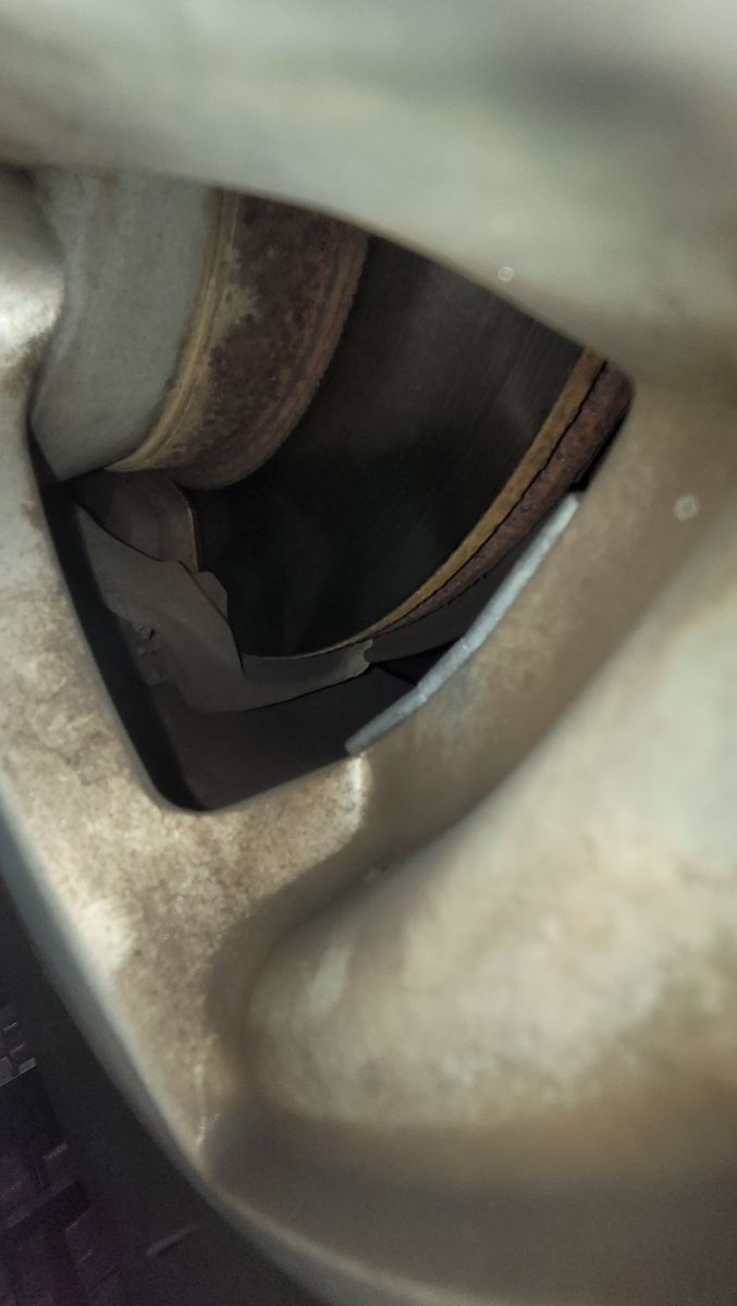View of worn car brake pads and rusty brake rotor through wheel