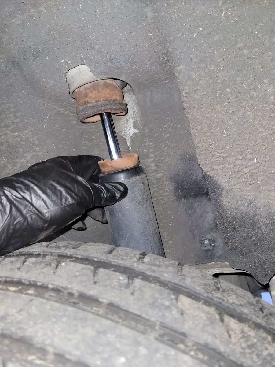 Close-up of a worn rubber bump stop above a car shock absorber near a tire.