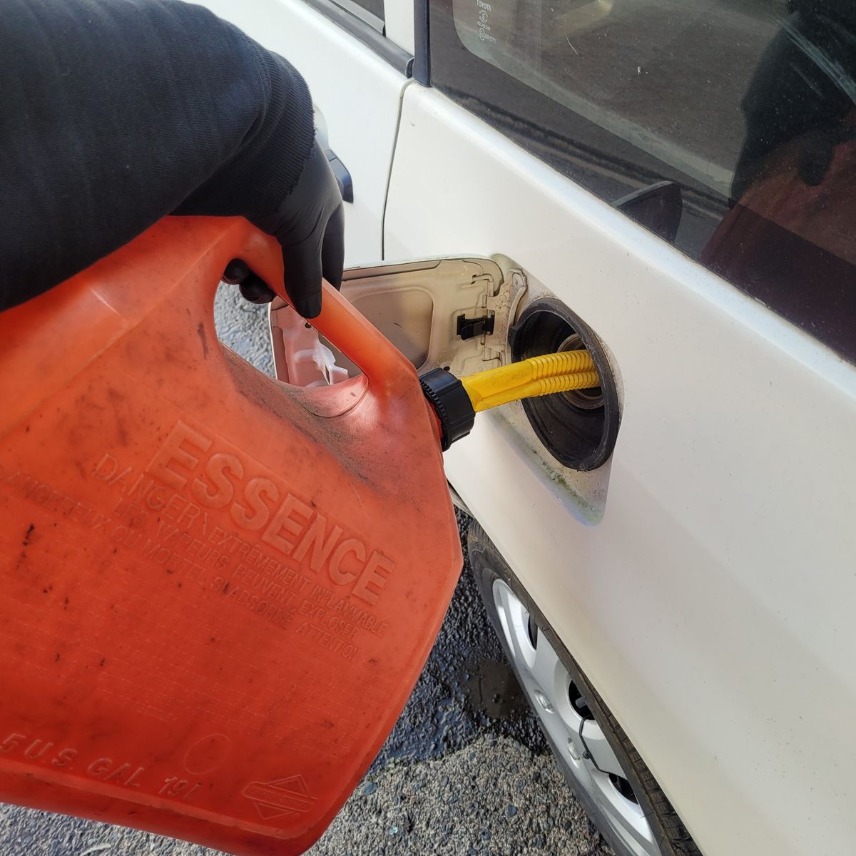 Pouring Gasoline from Red Fuel Container into Car Hand pouring gasoline from red fuel container into white car’s gas tank