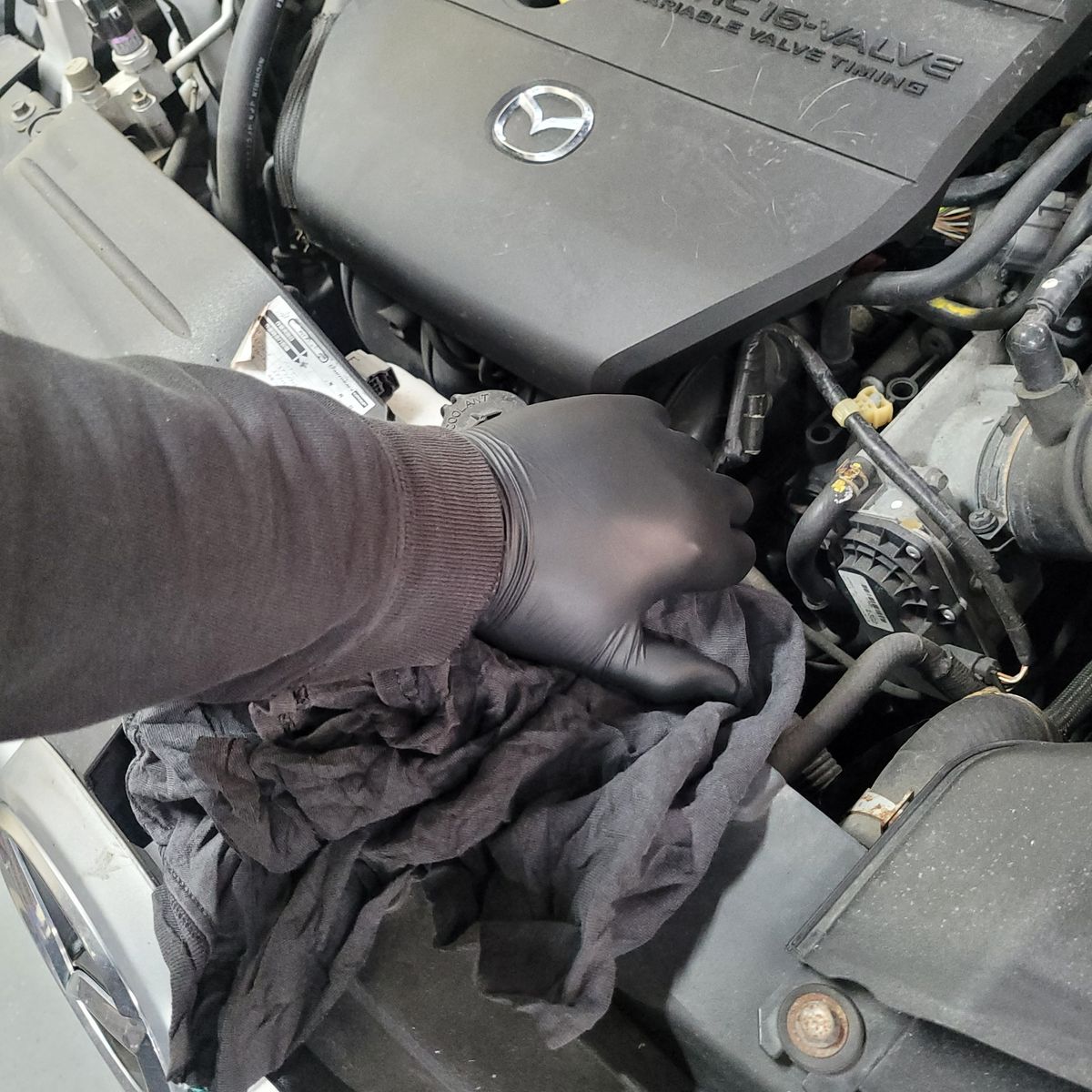 Hand Removing Radiator Cap on Mazda Engine Gloved hand removing radiator cap on Mazda engine with cloth