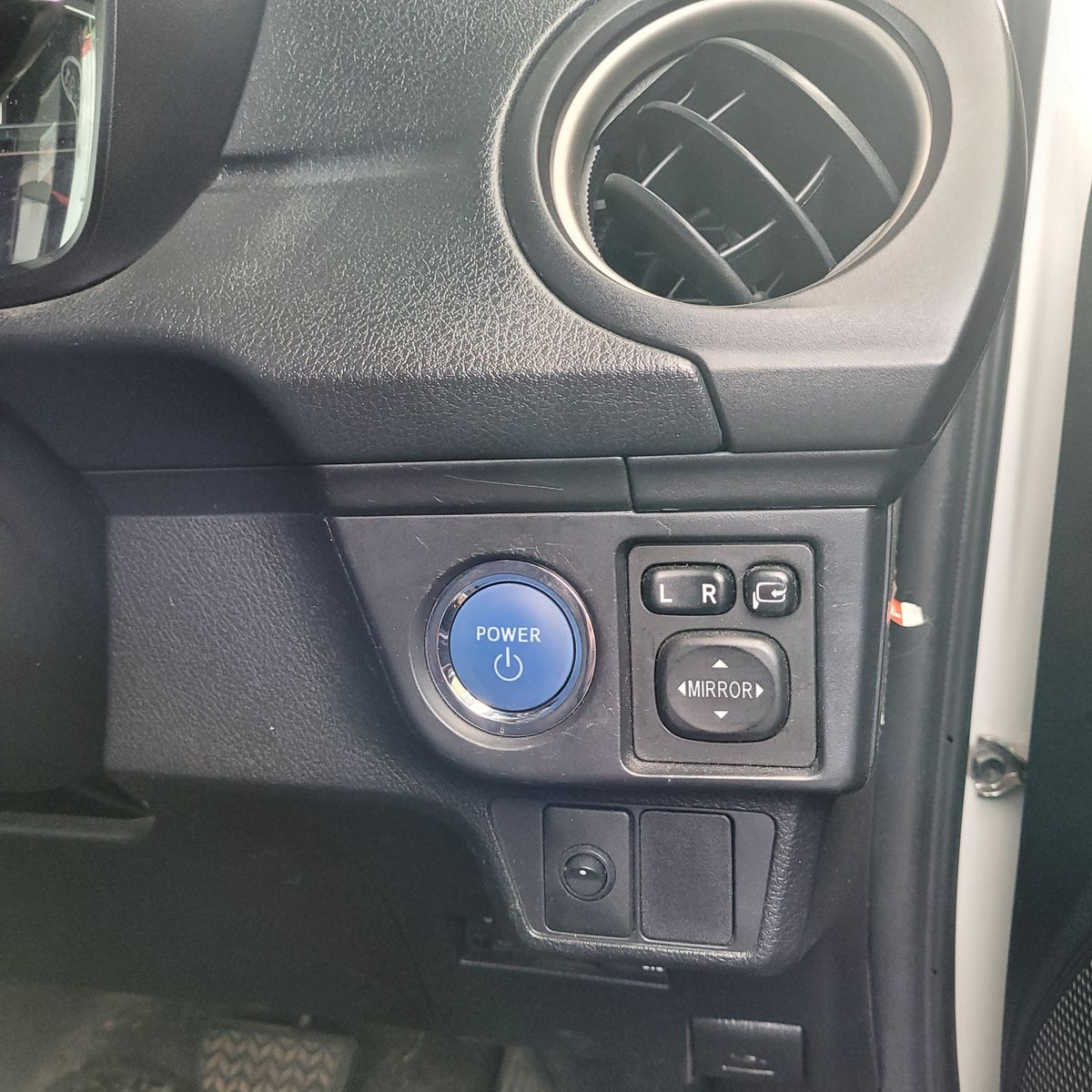 Blue power start stop button on vehicle dashboard beside mirror adjustment controls