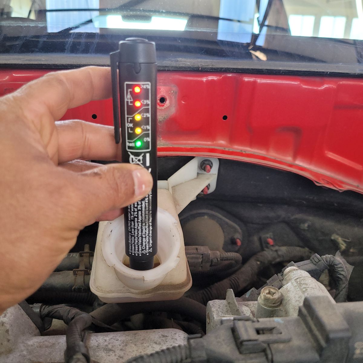Testing Brake Fluid Moisture with a Diagnostic Pen Hand using a brake fluid tester in a car's brake fluid reservoir