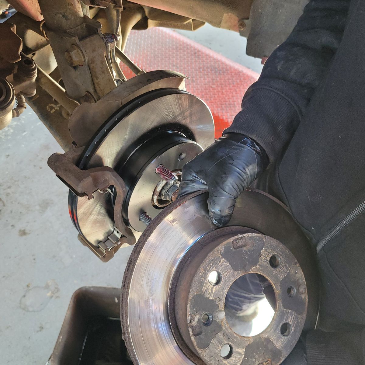 Old and New Brake Rotor Comparison During Replacement Gloved mechanic holding old brake rotor near newly installed rotor on vehicle