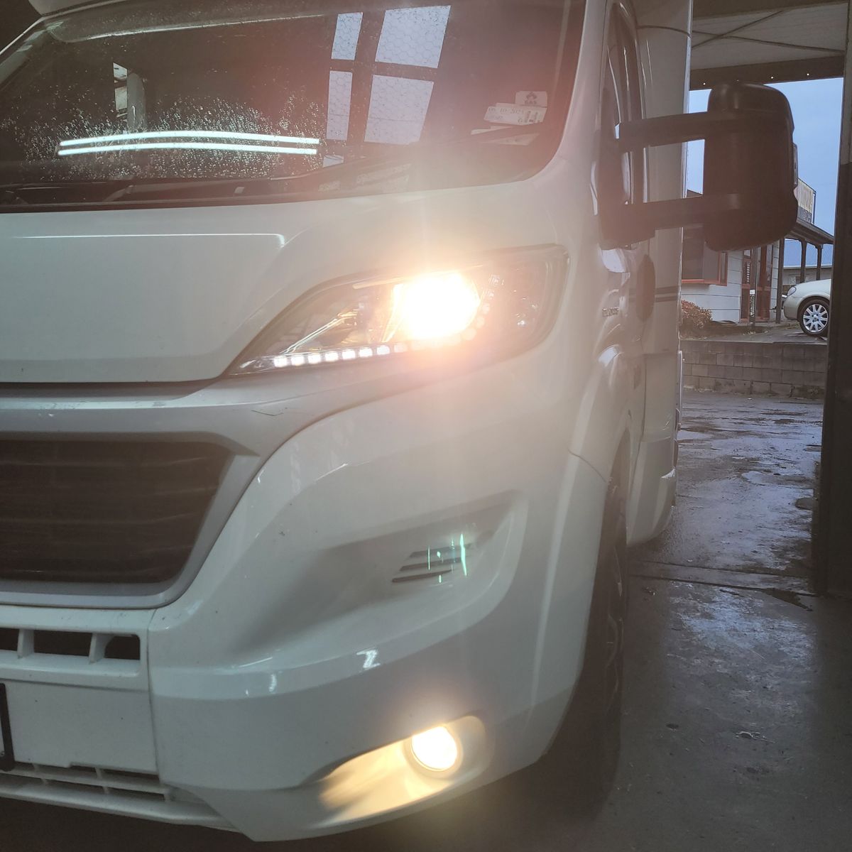 Front view of a white camper van with headlights and fog lights on