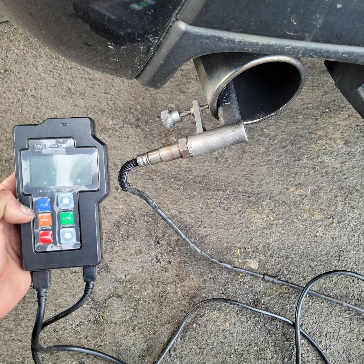 Emissions sensor attached to car exhaust, handheld analyzer reading test results.