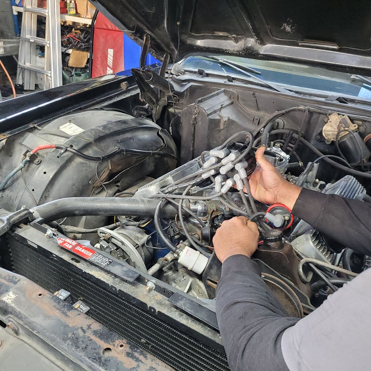 Mechanic inspecting spark plug wires under open car hood