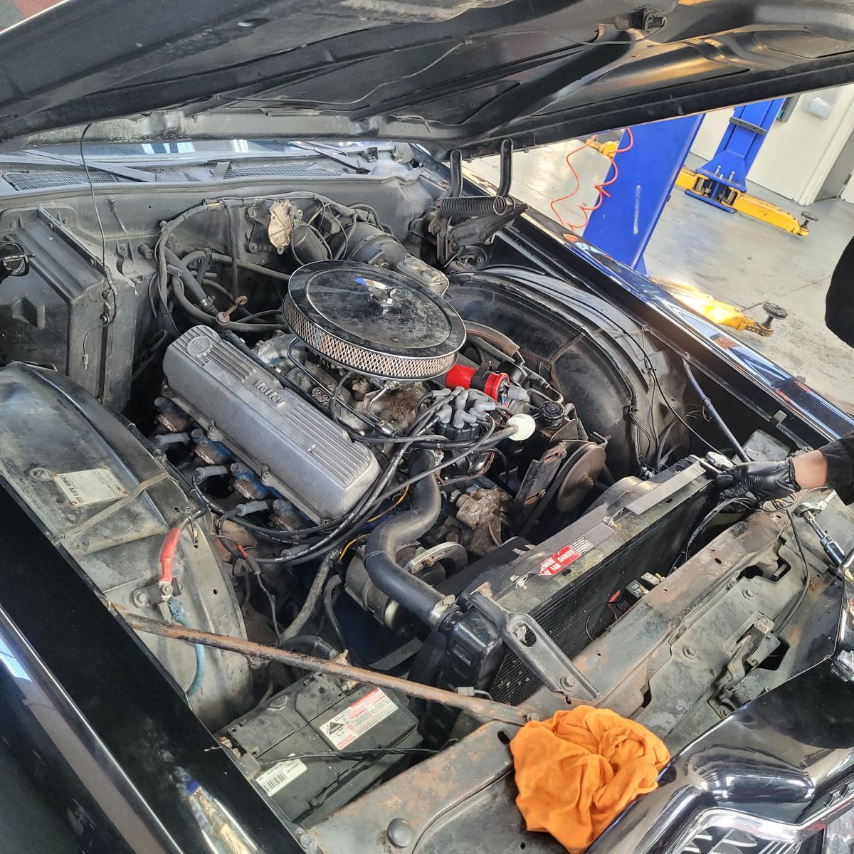 Exposed carburetted V8 engine bay with open hood in garage