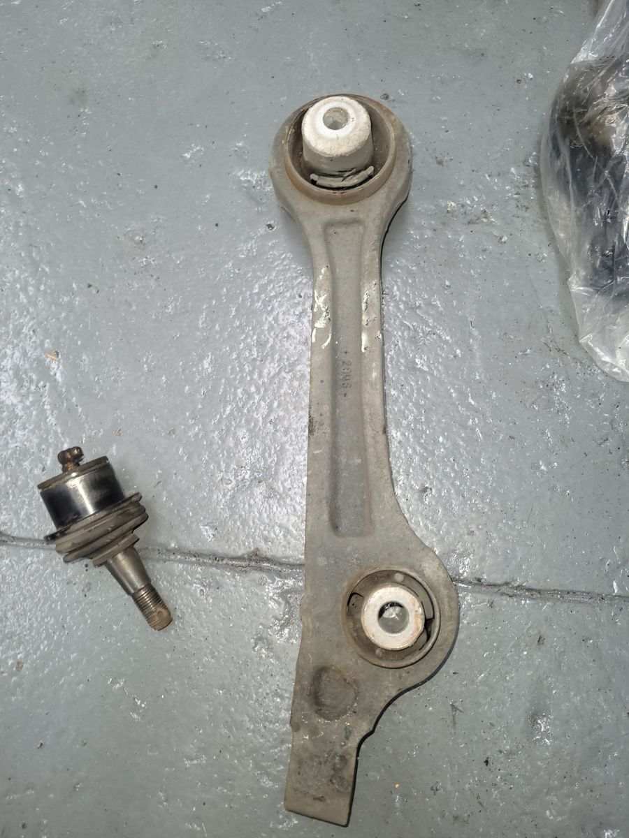 Metal control arm and ball joint lying on a gray concrete surface