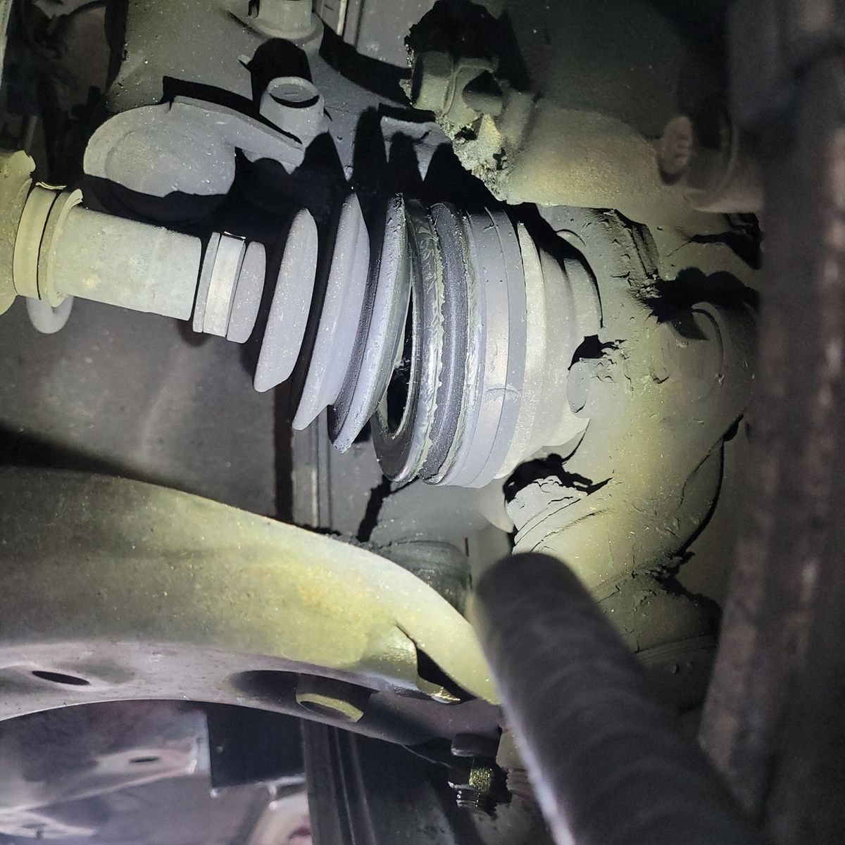 Damaged CV Boot on Vehicle Axle Close-up of torn CV boot with visible grease and axle parts.