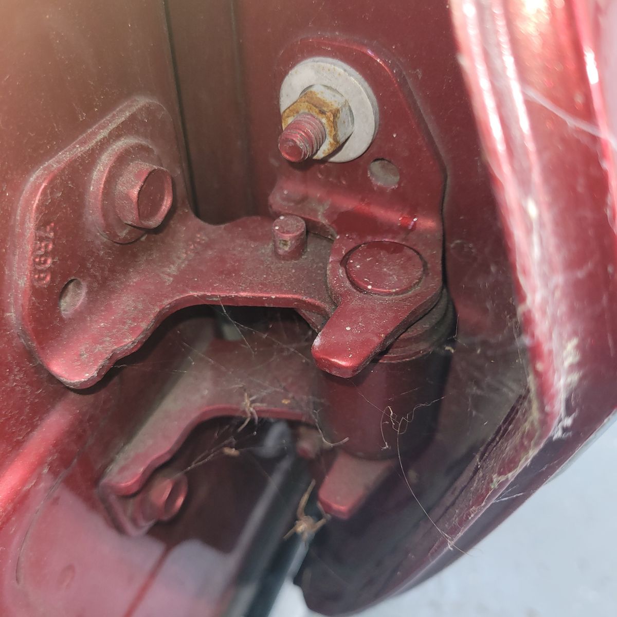 Detailed view of a maroon car door hinge with bolts and cobwebs.