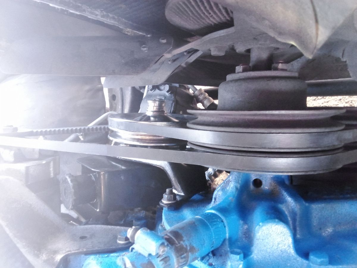 Drive belt wrapped around metal pulleys in a vehicle engine compartment.