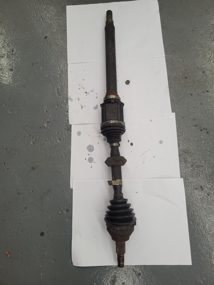 Used Automotive Drive Shaft on Workshop Floor A single worn drive shaft with rubber boots lying on a concrete floor.