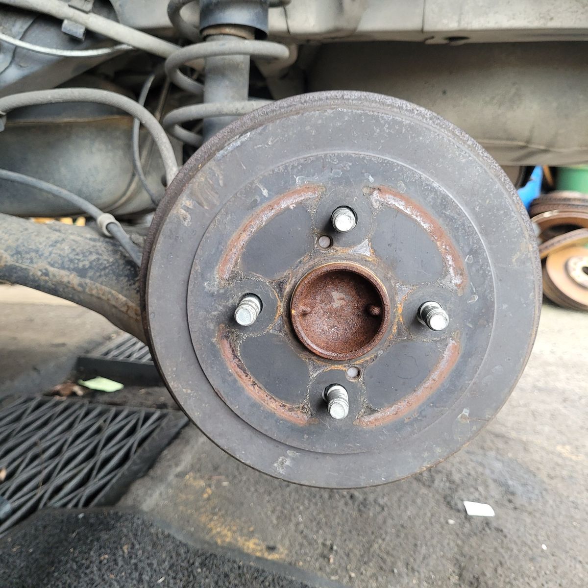 Close-Up View of a Car Drum Brake Assembly Car drum brake showing five wheel studs and rusty surface, attached to suspension.