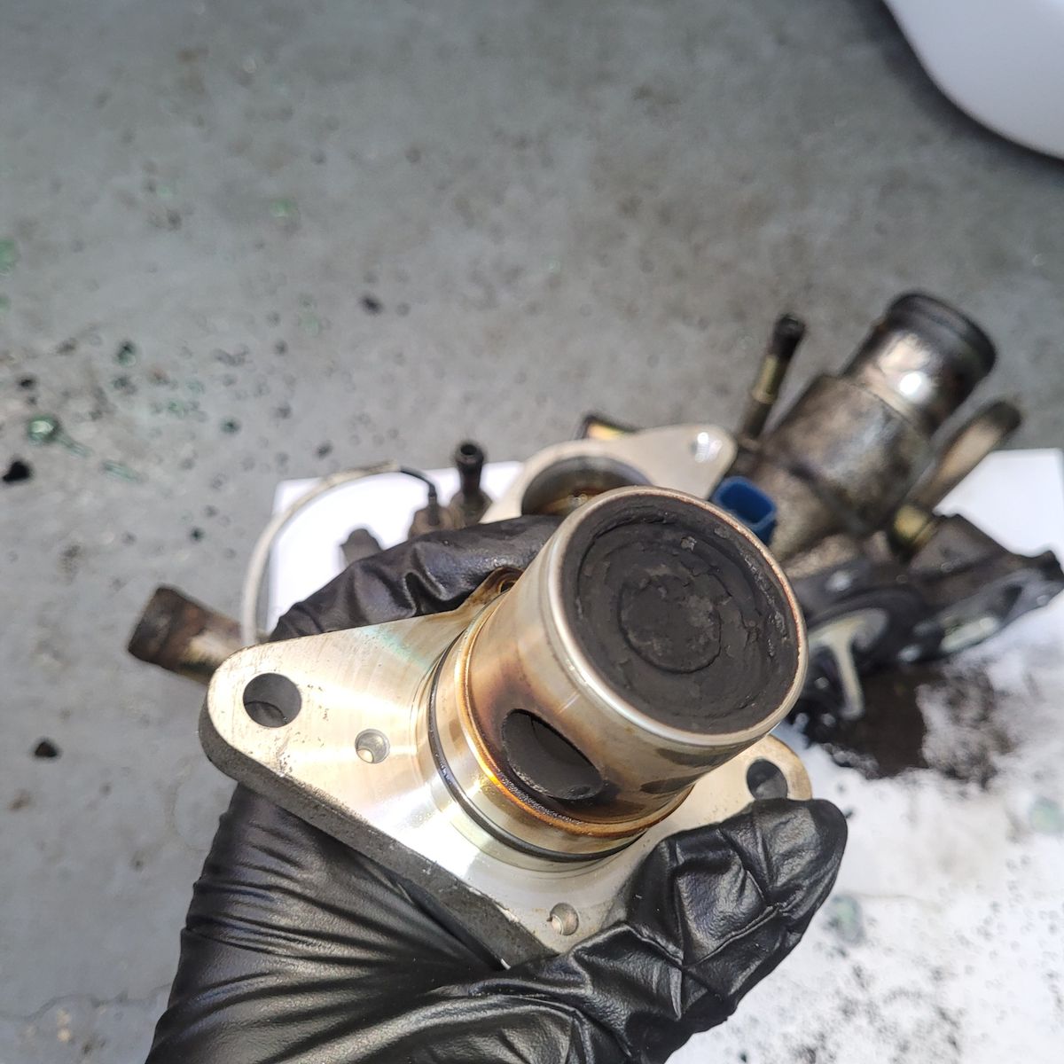 Dirty EGR valve with carbon buildup held in gloved hand