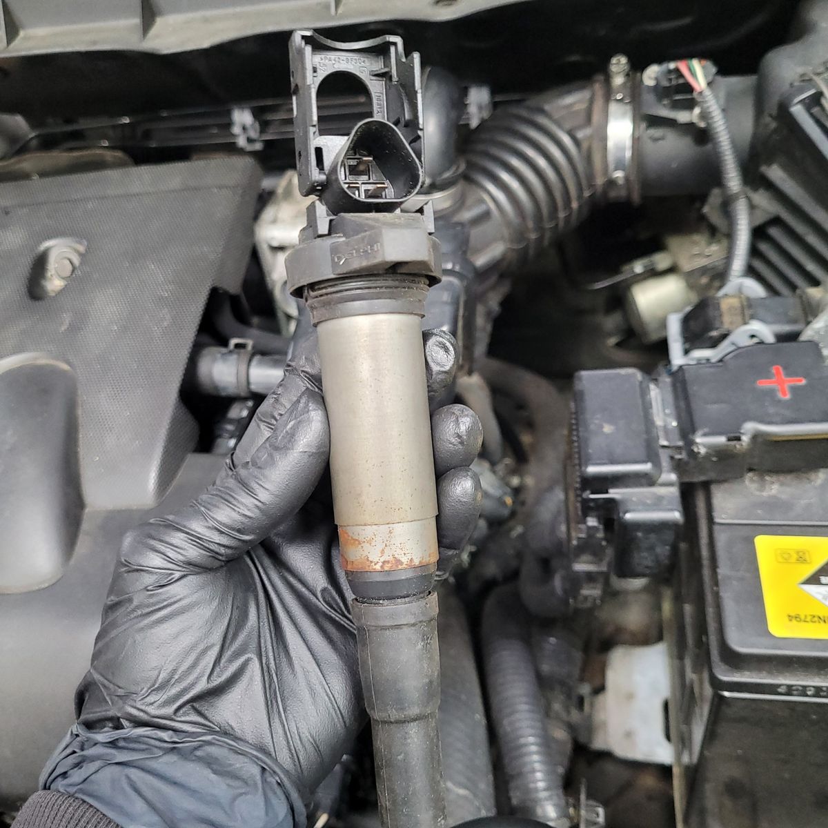 Mechanic holding an electronic ignition coil over a car engine bay