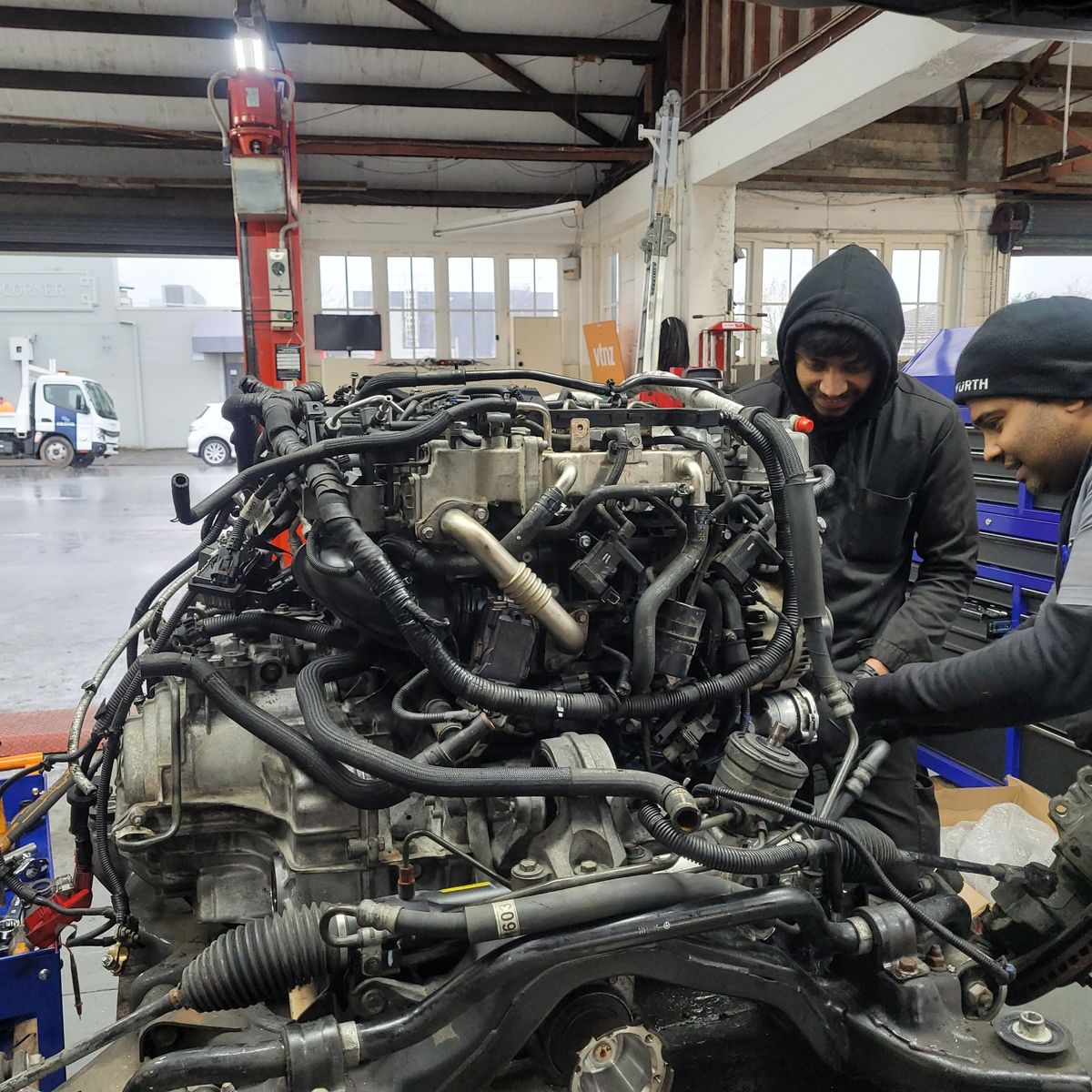 Mechanics Replacing Car Engine in Workshop Two mechanics installing a car engine in an auto repair shop