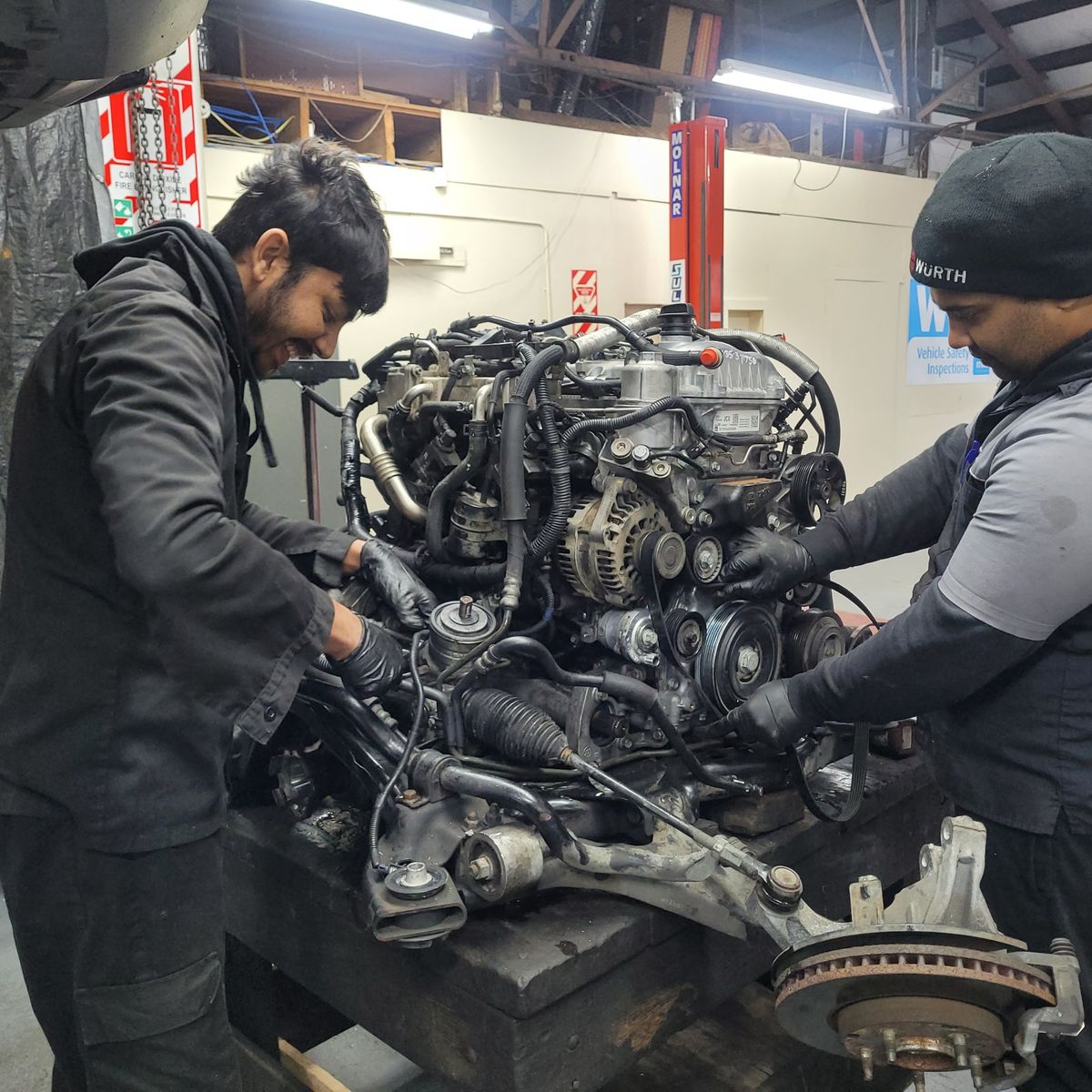 Mechanics Performing Engine Replacement in Auto Workshop Two mechanics working together to replace a car engine on a workbench.