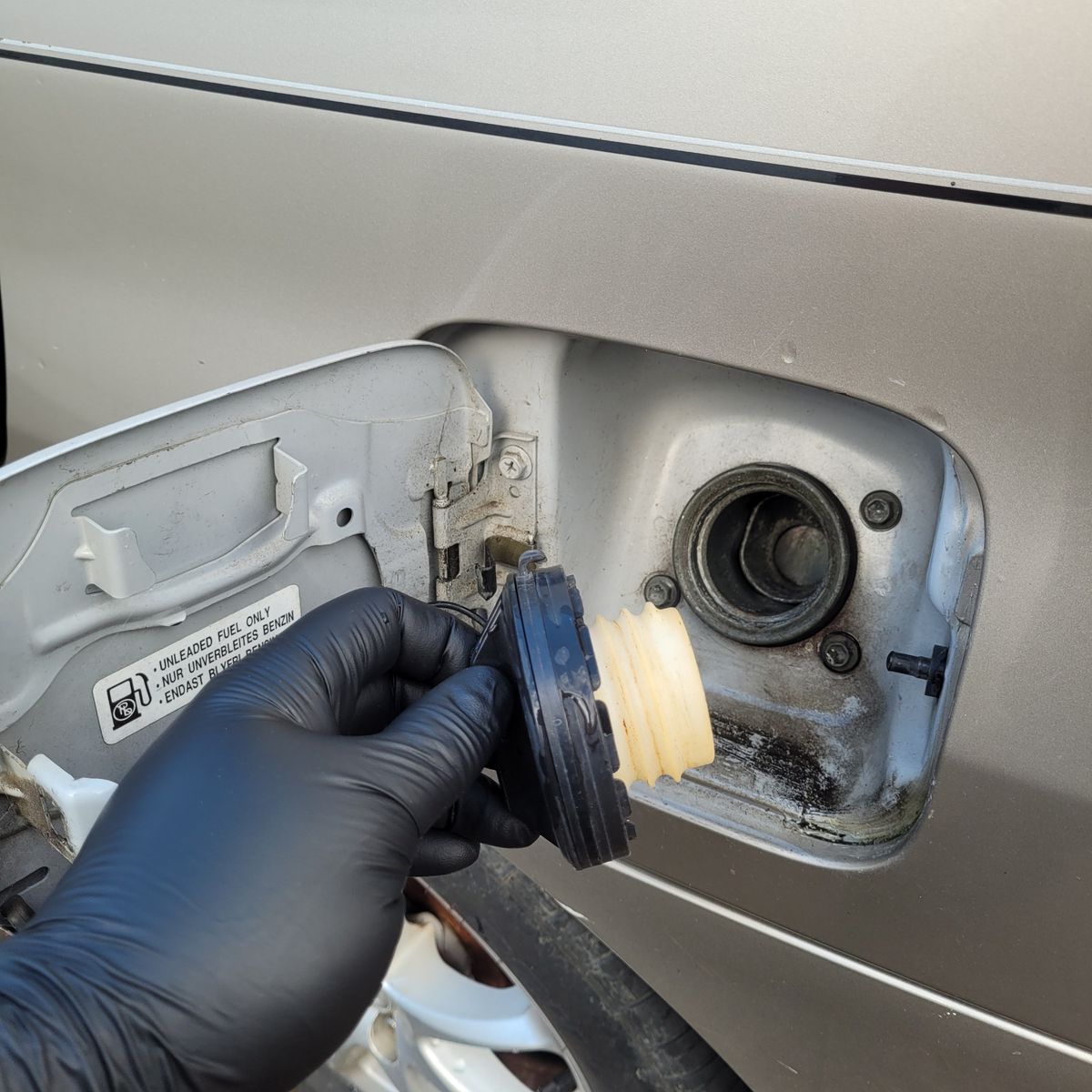 Fuel Cap Removal on Vehicle Gloved hand unscrewing fuel cap from car's fuel tank