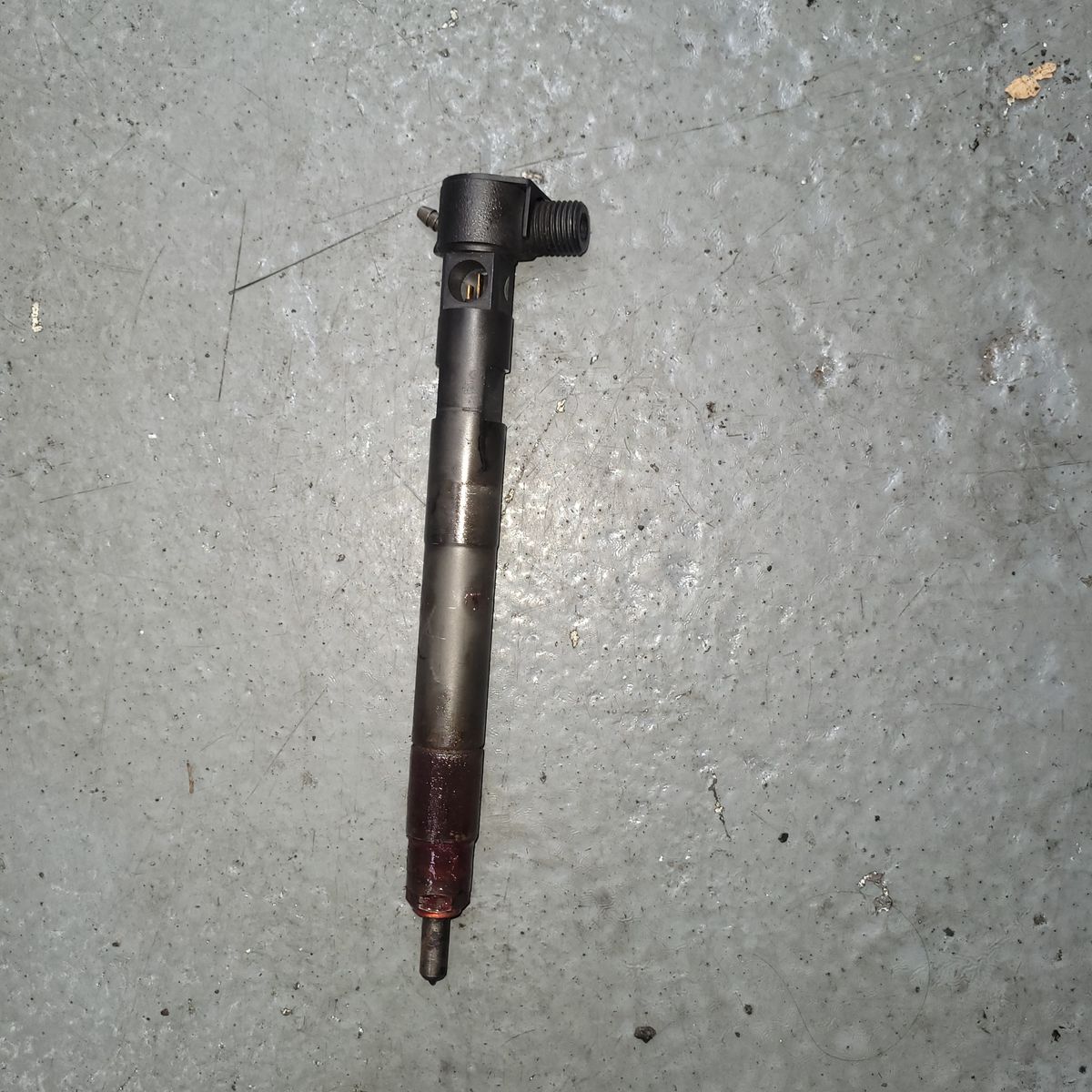 A single fuel injector lying on a grey, textured workshop floor.
