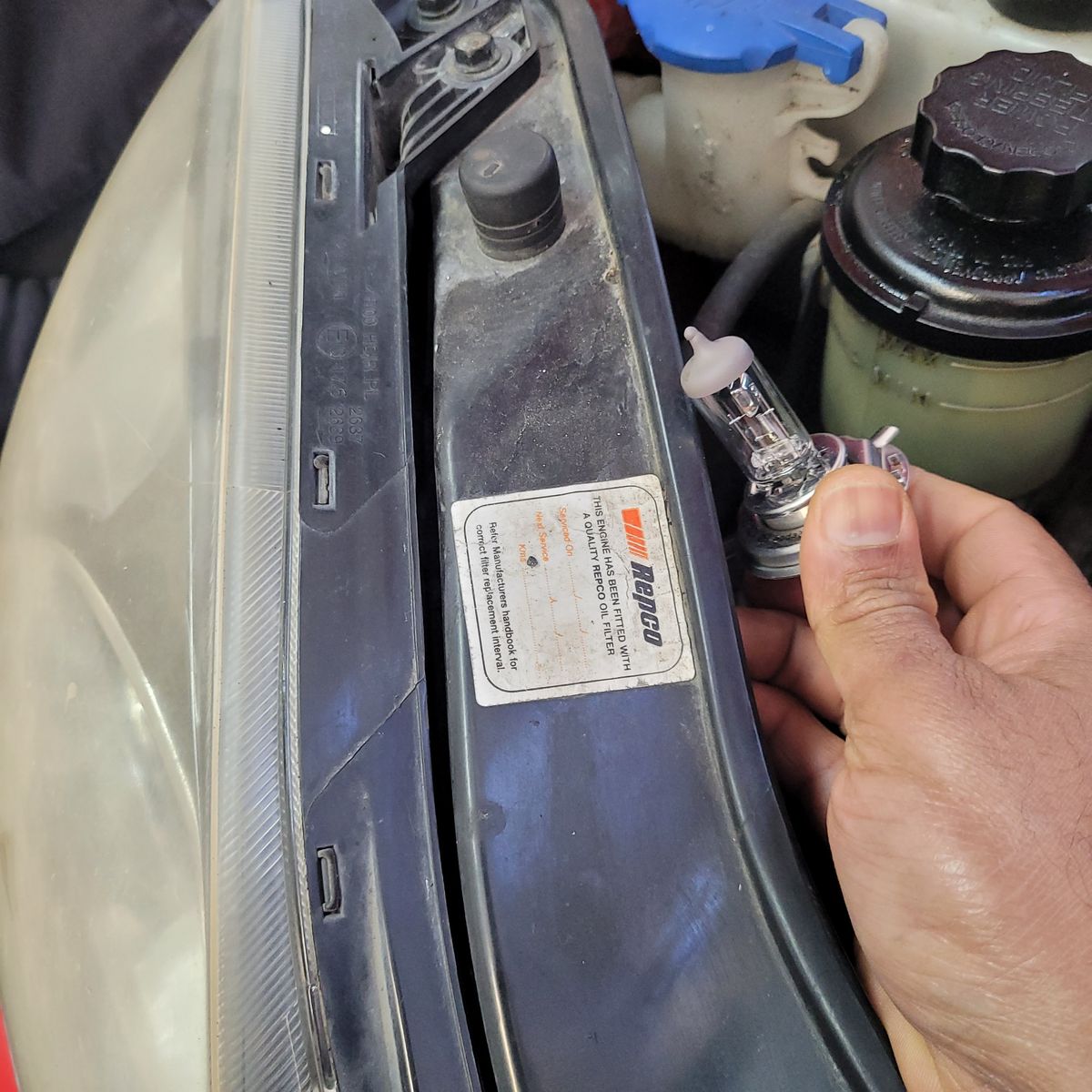 Installing a Halogen Headlight Bulb in Car Person holding a halogen headlight bulb next to a car headlamp assembly.