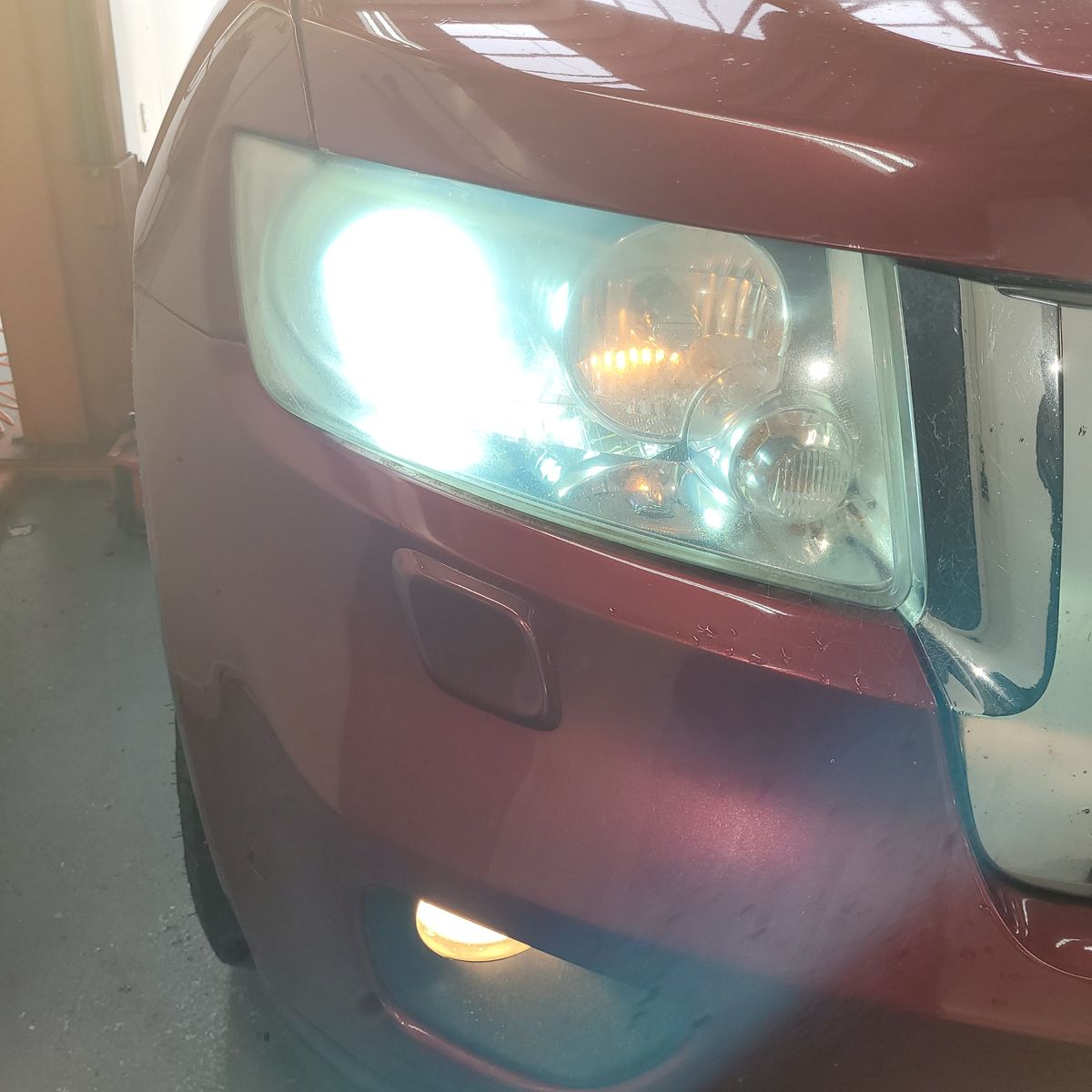 Close-up of a car's dim, foggy headlight on a maroon vehicle