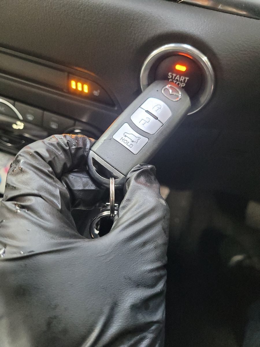 Car Key Fob Held to Push Start Button Gloved hand holding a Mazda key fob near a car's push start button