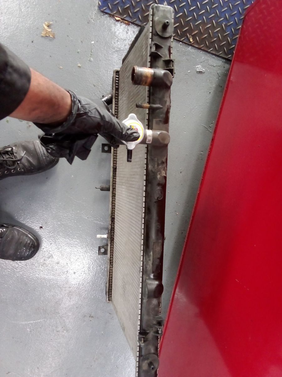 Mechanic Holding Car Radiator by Cap Gloved hand holds the cap of an upright car radiator in a garage.