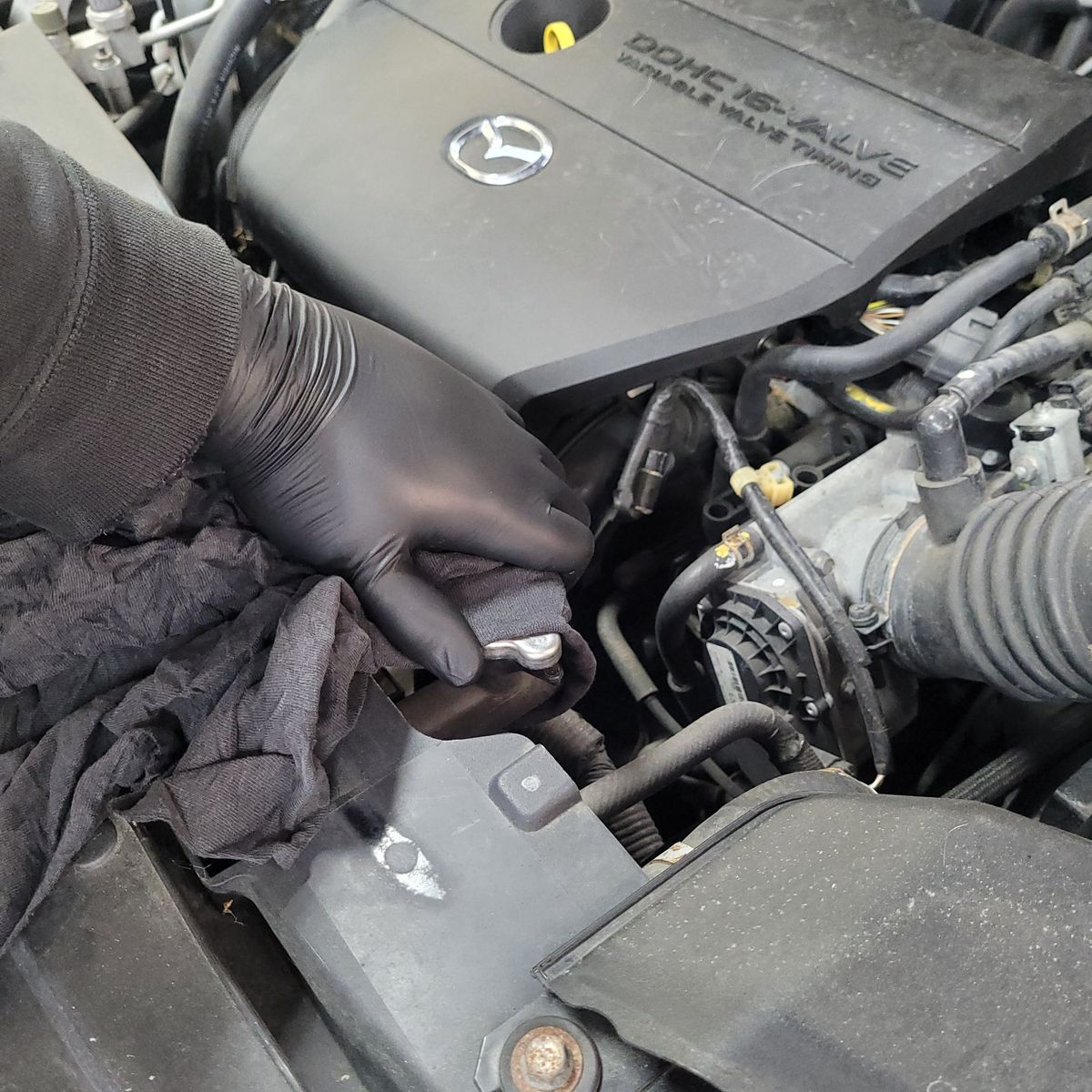 Gloved hand removing a radiator cap from a Mazda engine bay