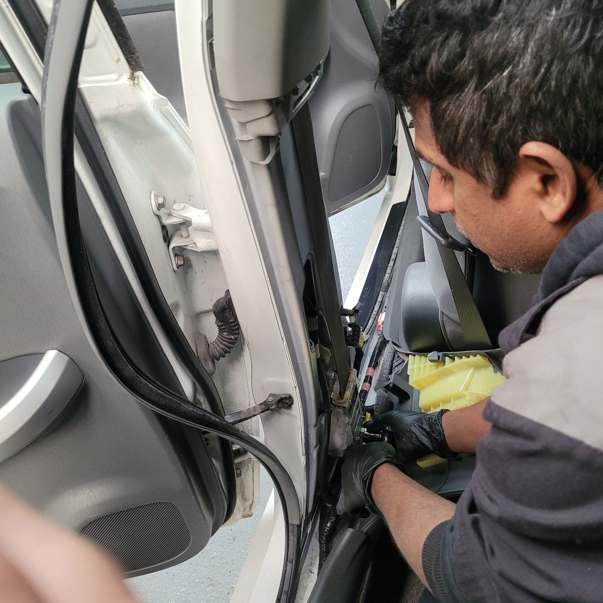 Technician Removing Car Seat Belt Assembly Mechanic carefully detaching seat belt assembly from car's interior frame.