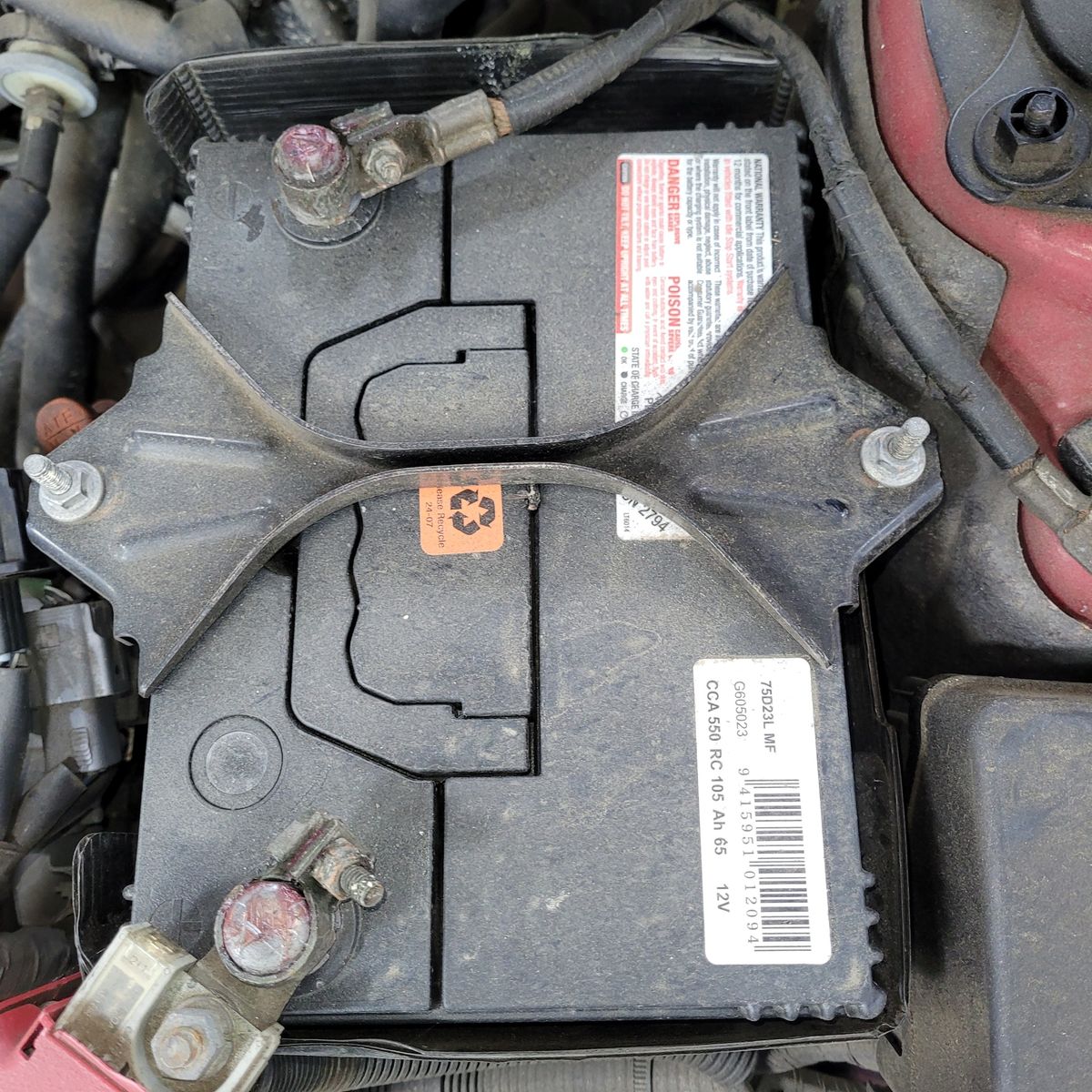 Secured 12V Car Battery in Engine Bay Dusty 12V car battery secured by a metal bracket in an engine compartment.