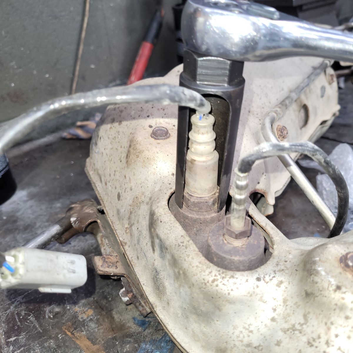 Removing an Oxygen Sensor from Exhaust Manifold Oxygen sensor being removed from a car exhaust manifold with a socket wrench.
