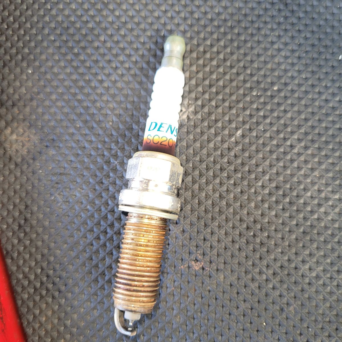 Close-up of a single used spark plug on a black rubber mat.