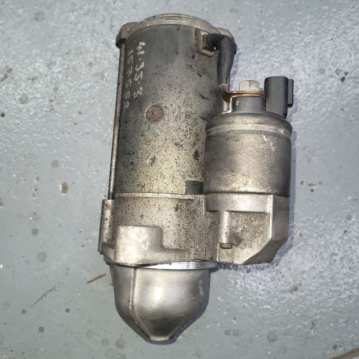 Used Automotive Starter Motor on Workshop Floor Old, slightly dirty starter motor placed on a gray workshop floor