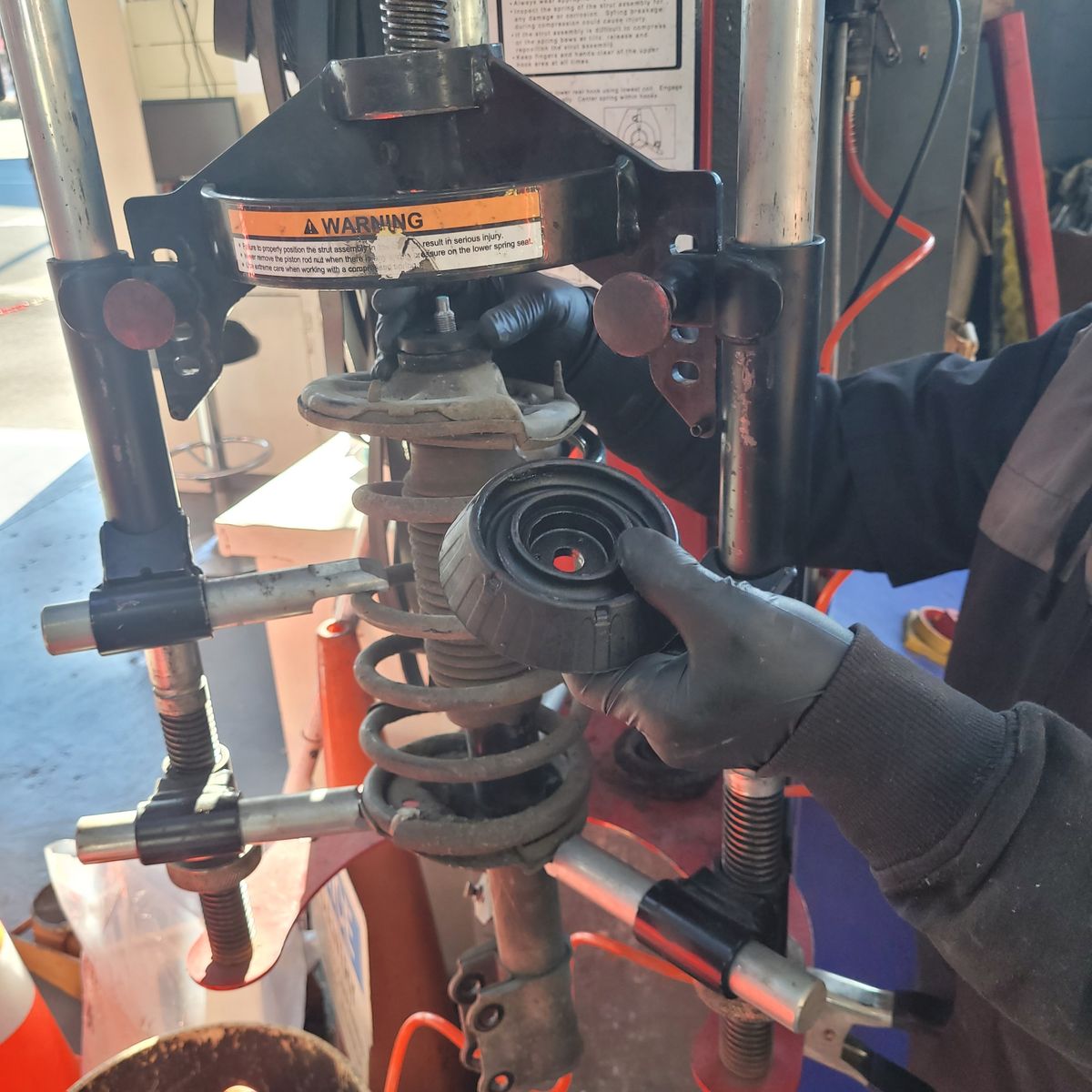 Mechanic Replacing Car Strut Mount on Spring Compressor Gloved hands holding a strut mount over a compressed car suspension spring.