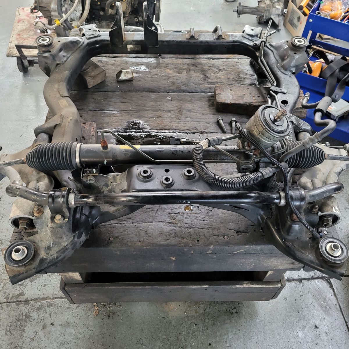 Automotive Subframe with Steering Rack A metal automotive subframe with attached steering rack on a workshop bench