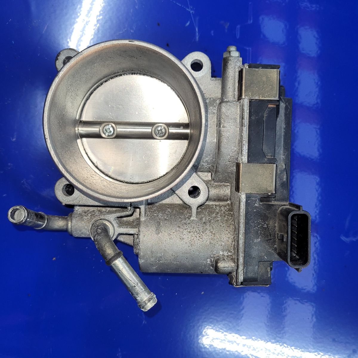 Automotive Throttle Body on Blue Surface Clean metal throttle body unit with electronic connector and vacuum ports