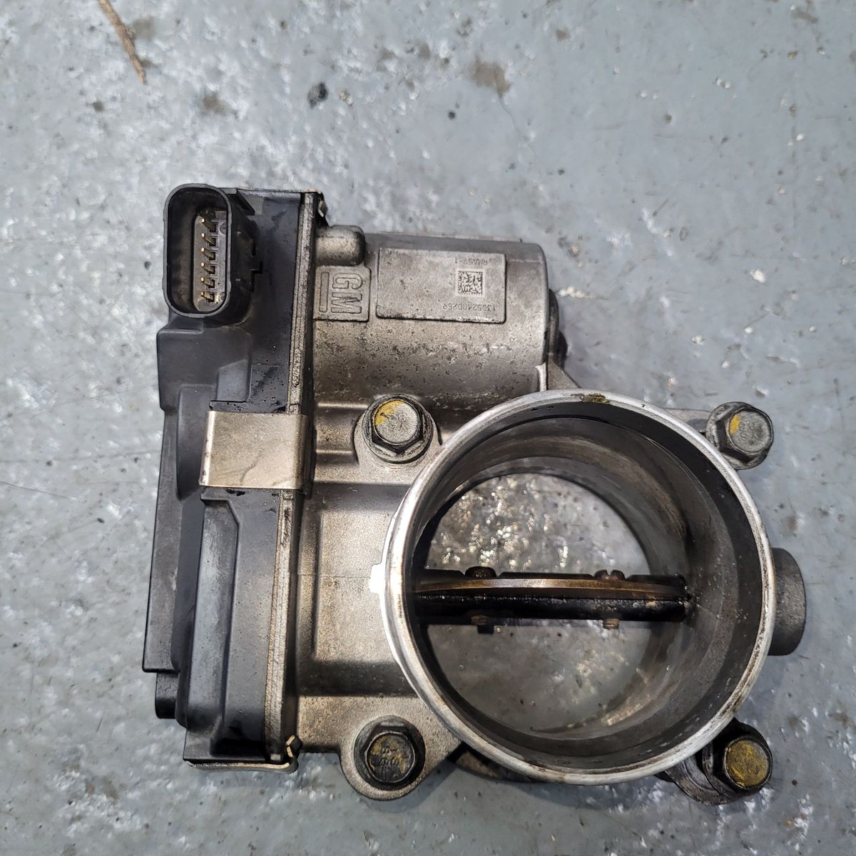 Closeup of a GM electronic throttle body on a gray concrete floor