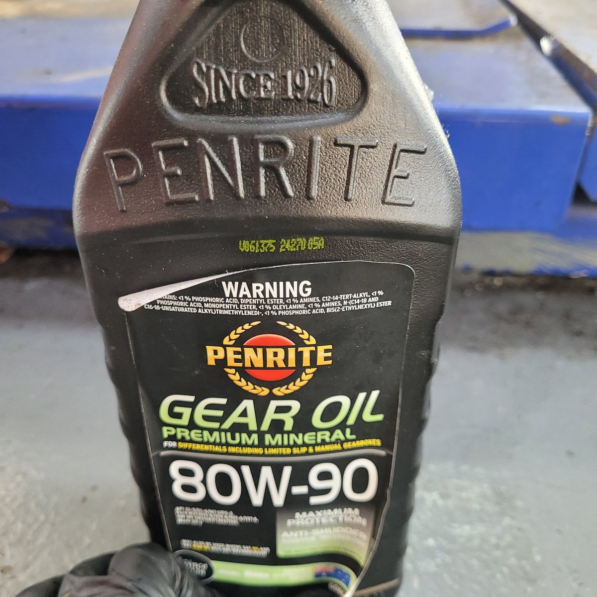 Hand holding Penrite Gear Oil 80W-90 bottle on workshop floor.