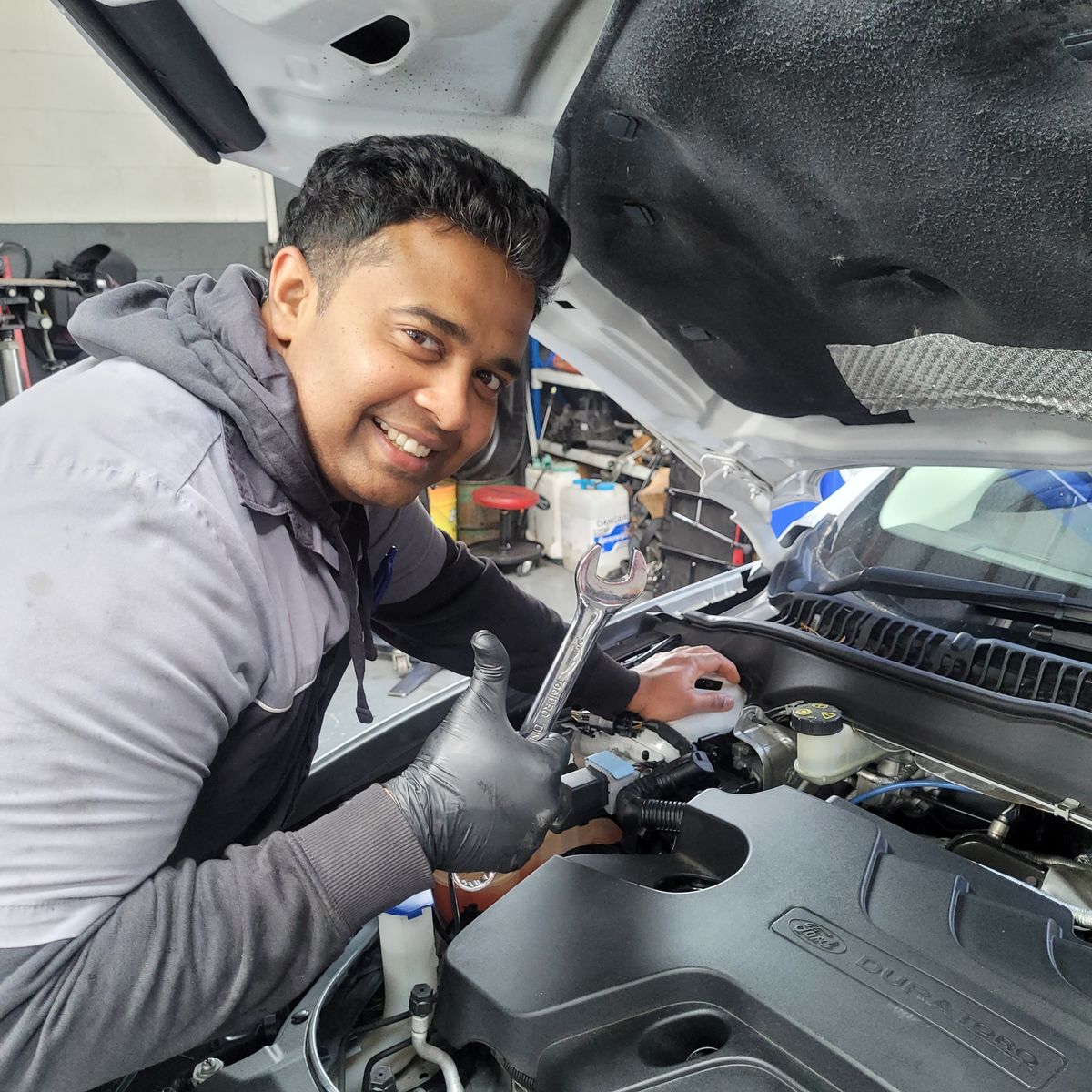Friendly Mechanic Working on Car Engine Smiling mechanic in gloves gives a thumbs up while fixing a car engine.