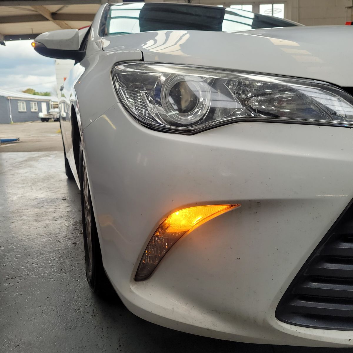Close-up of a white car's front turn signal illuminated