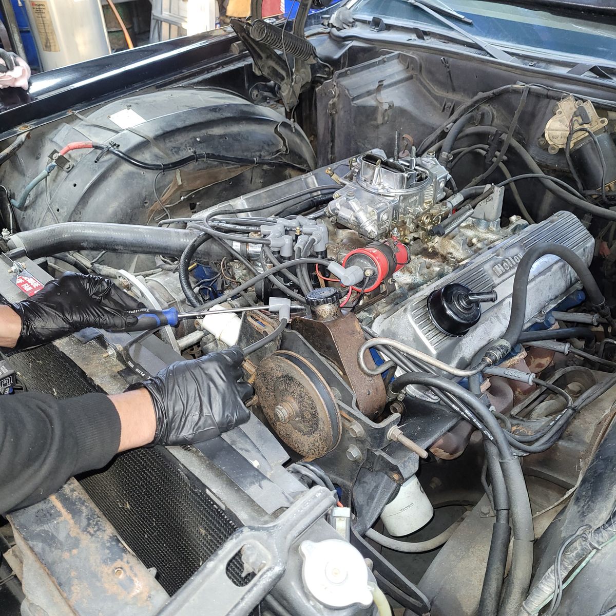 Mechanic Troubleshooting Car Engine Issues Gloved hands using tools to work on a car engine in an open hood.