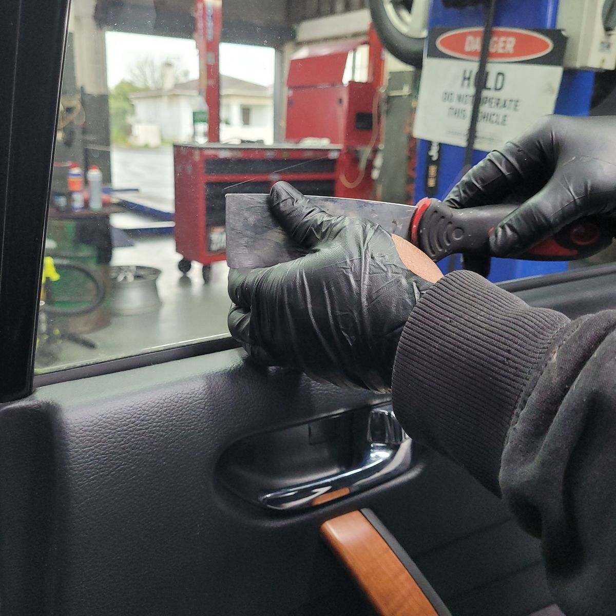 Professional Window Tinting Application in Auto Shop Gloved hands applying window tint film inside a car door at a garage.
