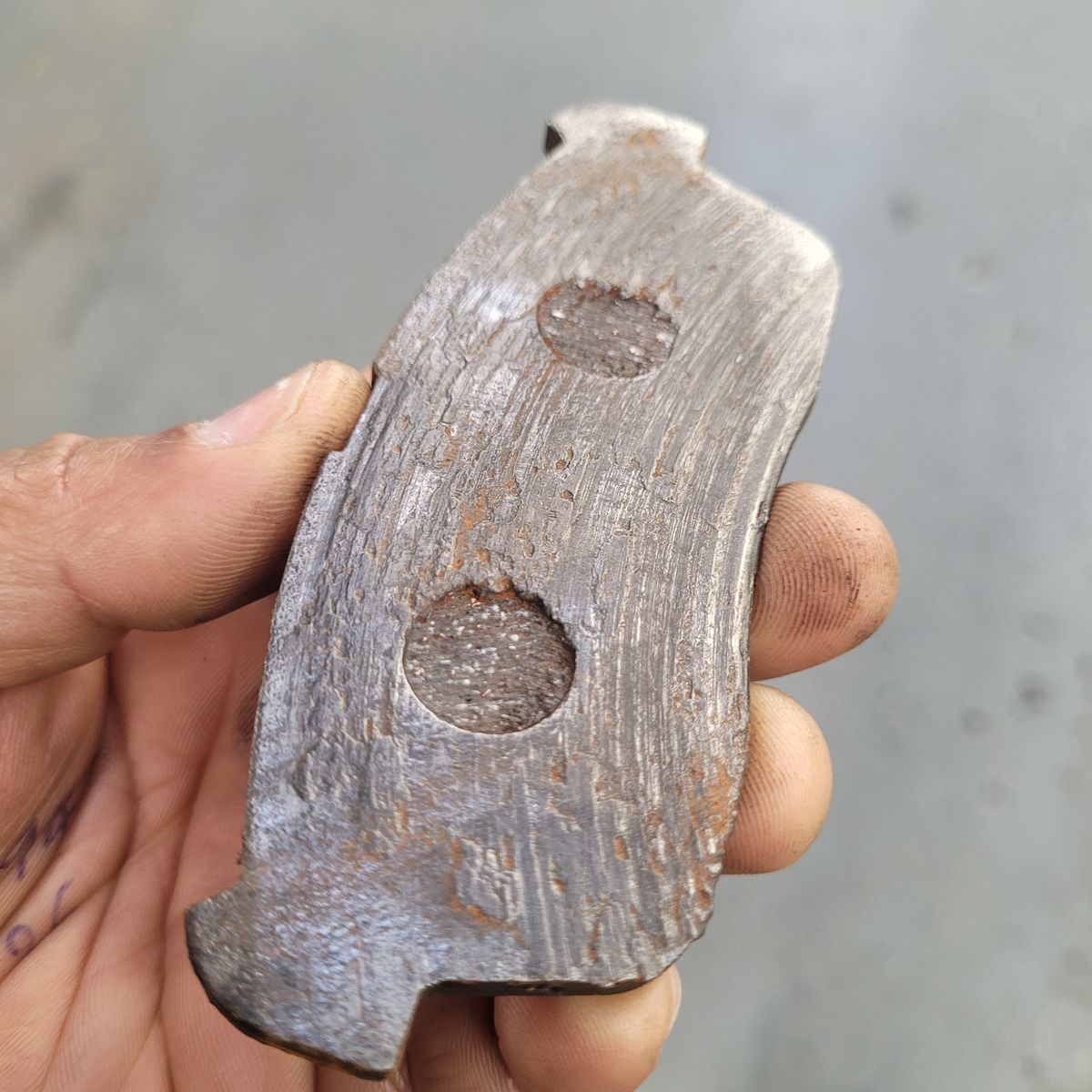 Worn-Out Brake Pad Close-Up Hand holding a heavily worn brake pad with deep grooves and rust.