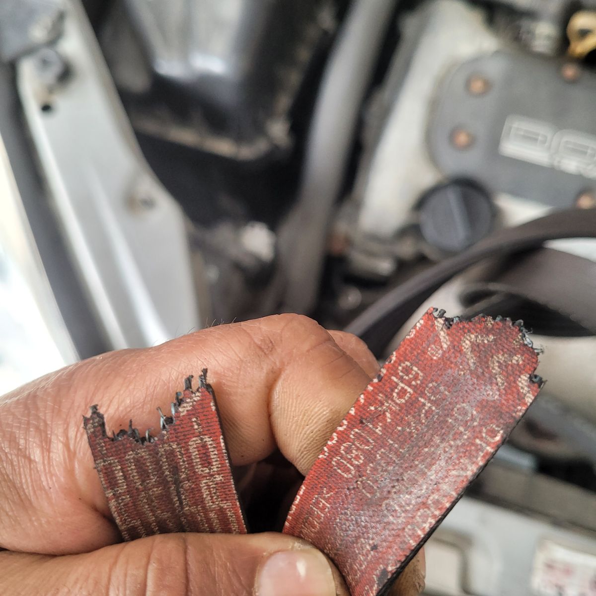 Broken Car Belt Causing Burning Smell Mechanic holding a frayed, burnt car belt beside engine